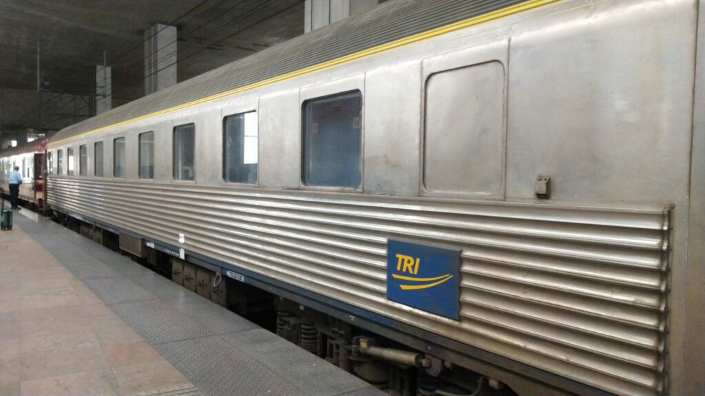 Ein grauer Wagon mit Alu/Blech-Verkleidung am Bahnsteig.