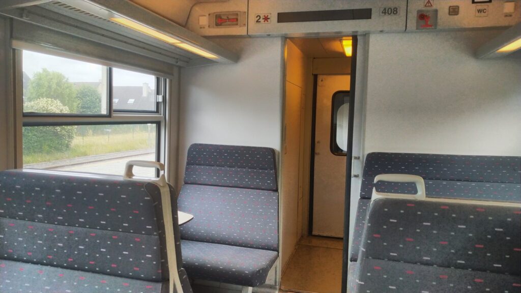 Innenansicht in einem Zug. Links und rechts sind Sitzgruppen. Links 4er, rechts 6er.